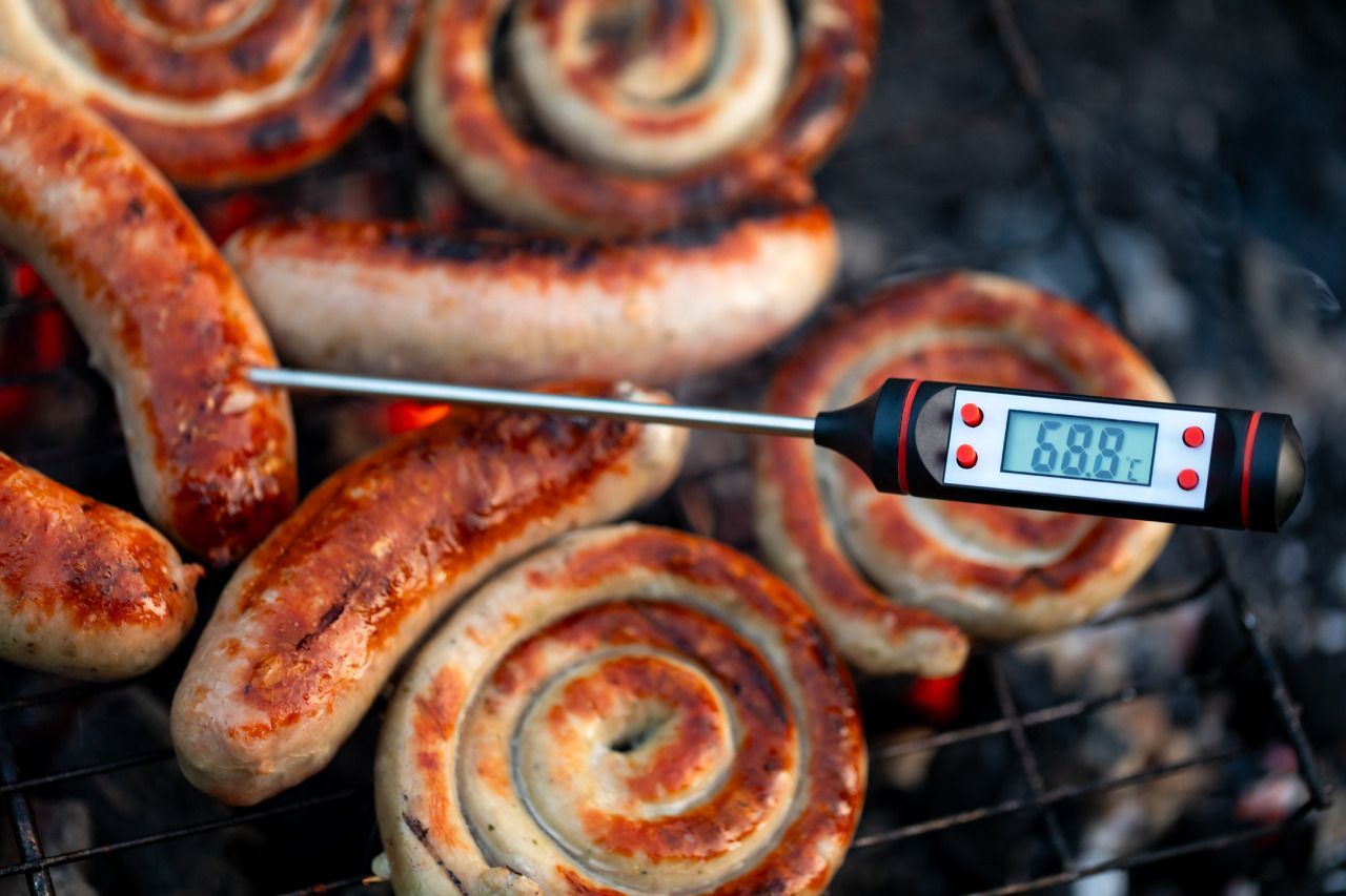 Um termômetro está sendo usado para verificar a temperatura de salsichas na grelha.