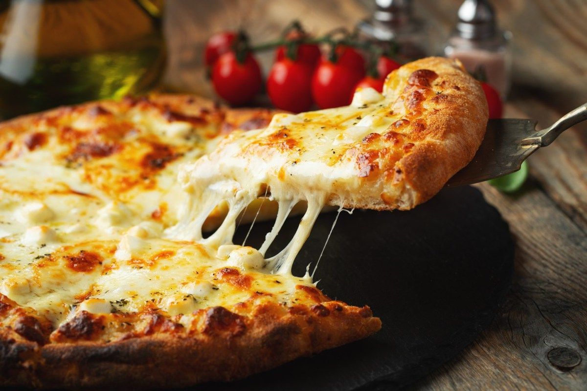 Uma pizza com uma fatia retirada dela sobre uma mesa de madeira.