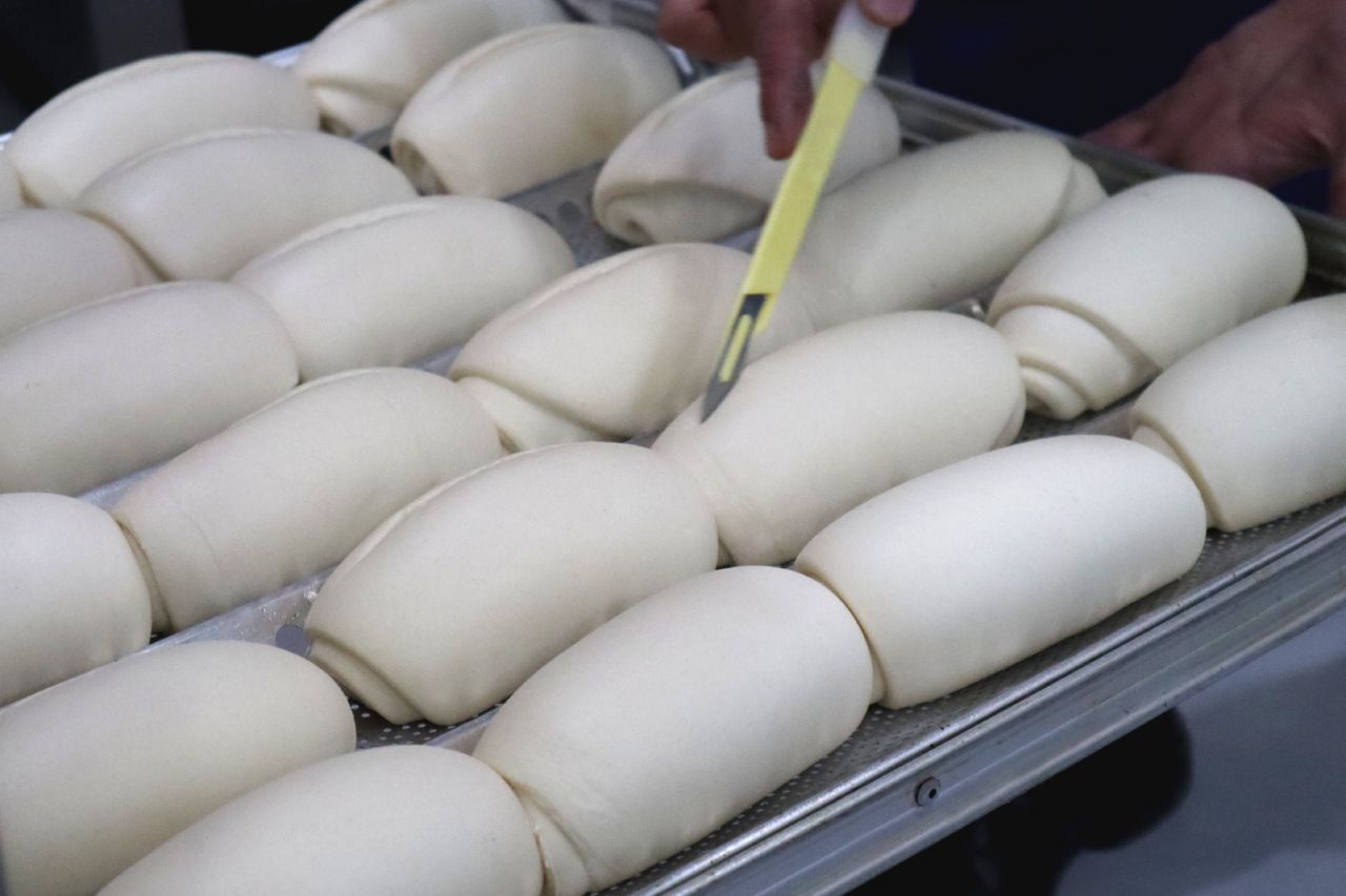 pães franceses crus fermentados sendo riscados antes de ir ao forno