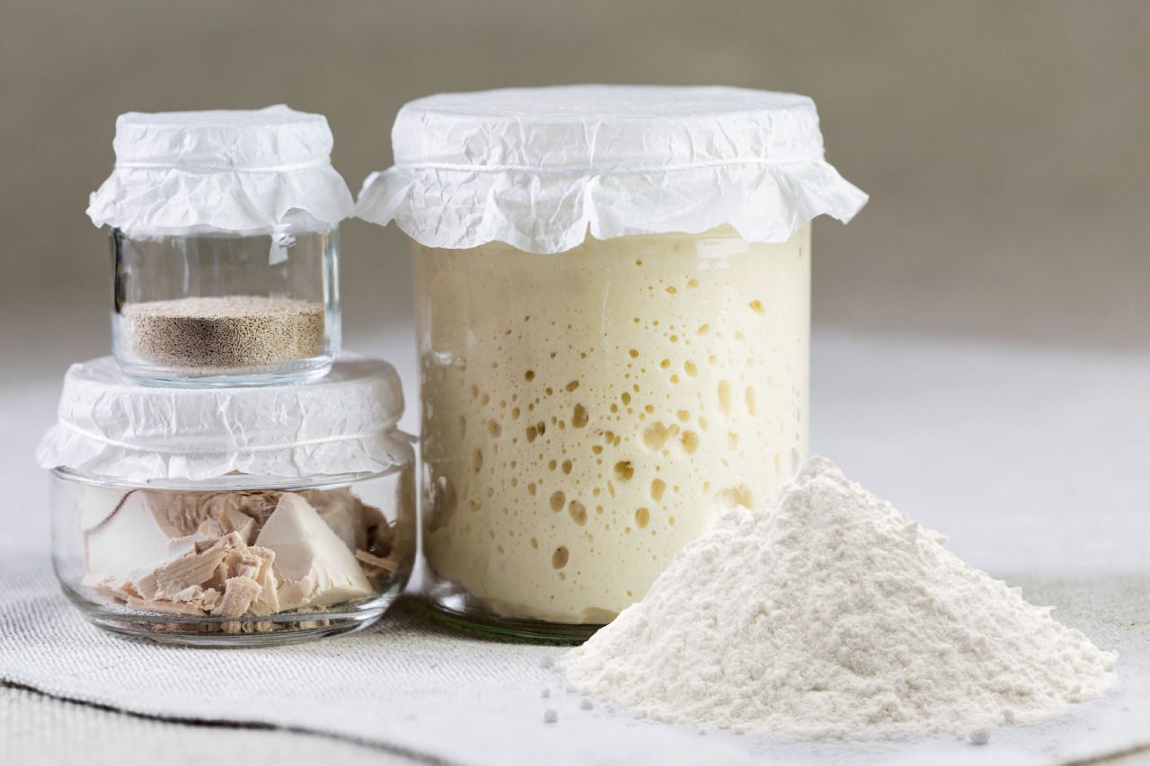 Um pote de fermento natural ao lado de uma pilha de farinha.