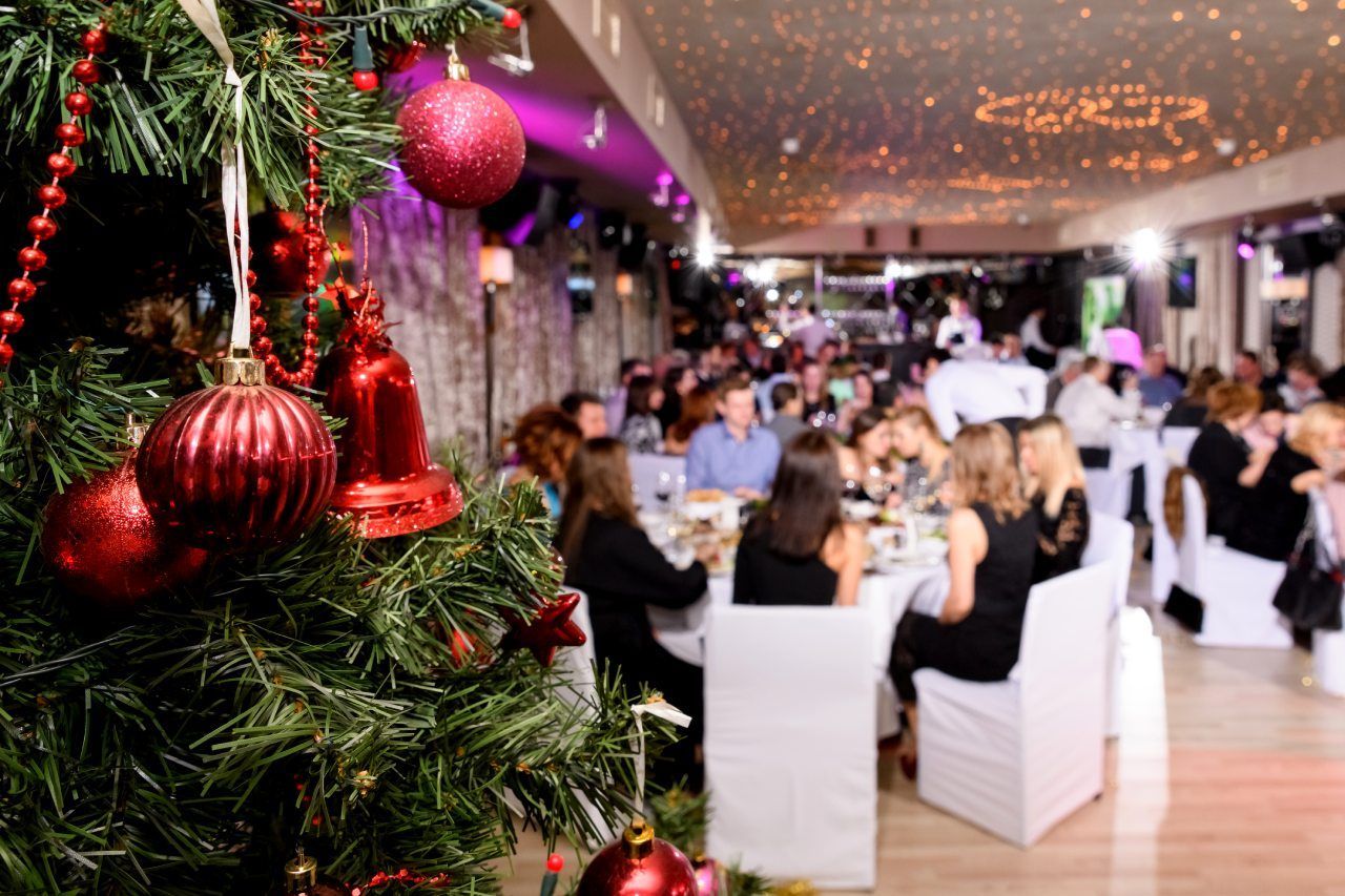 Um grupo de pessoas está sentado em mesas em um restaurante com uma árvore de natal em primeiro plano.