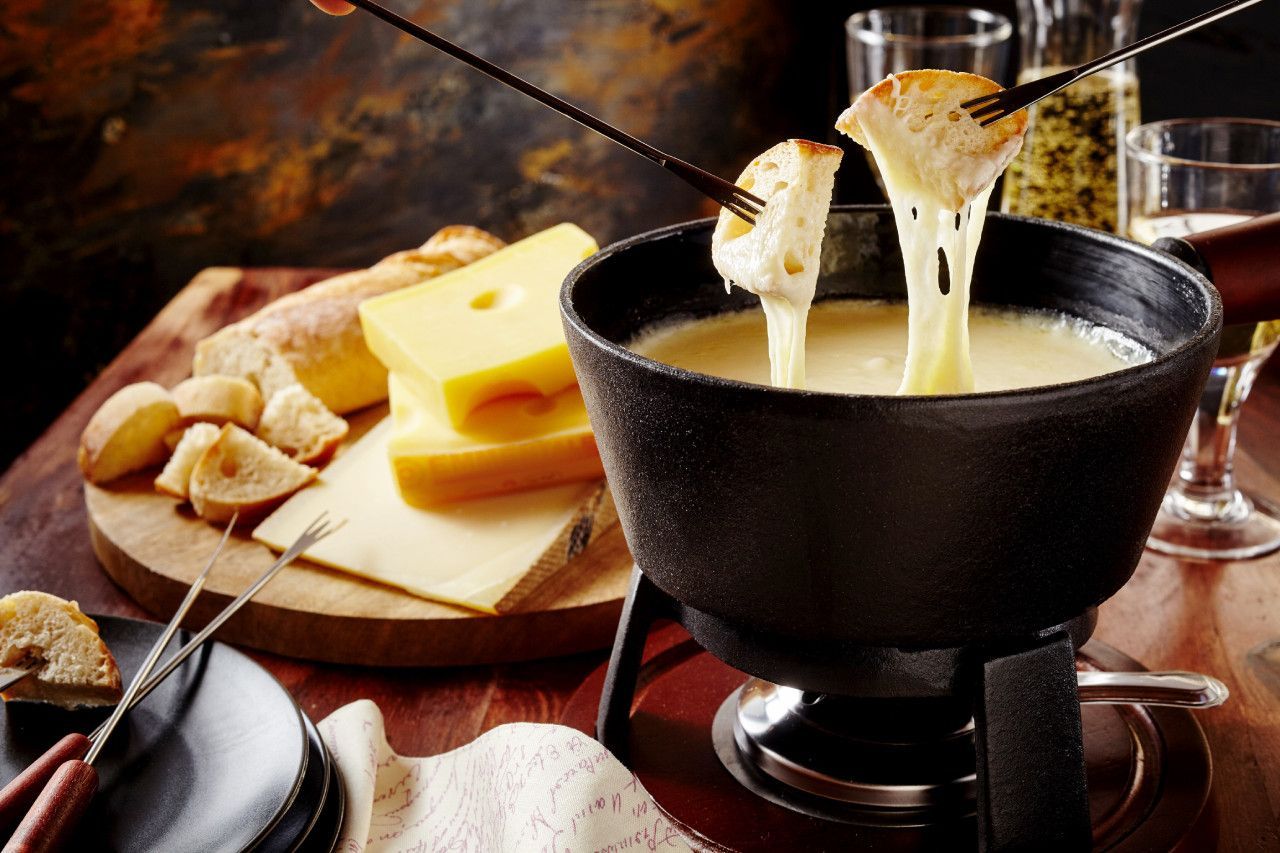 Uma pessoa está mergulhando um pedaço de pão em uma tigela de fondue de queijo.
