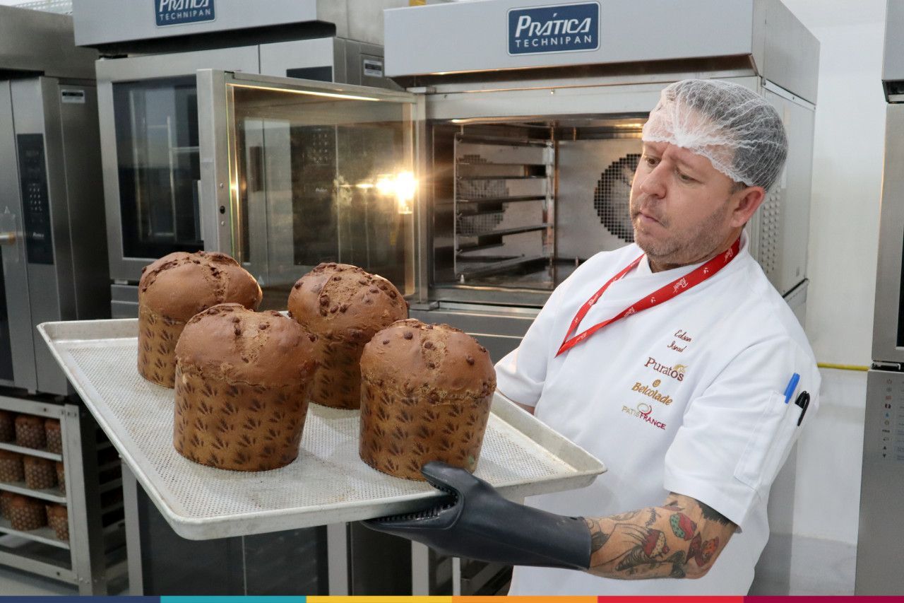 Um homem está segurando uma bandeja de cupcakes em frente ao forno.