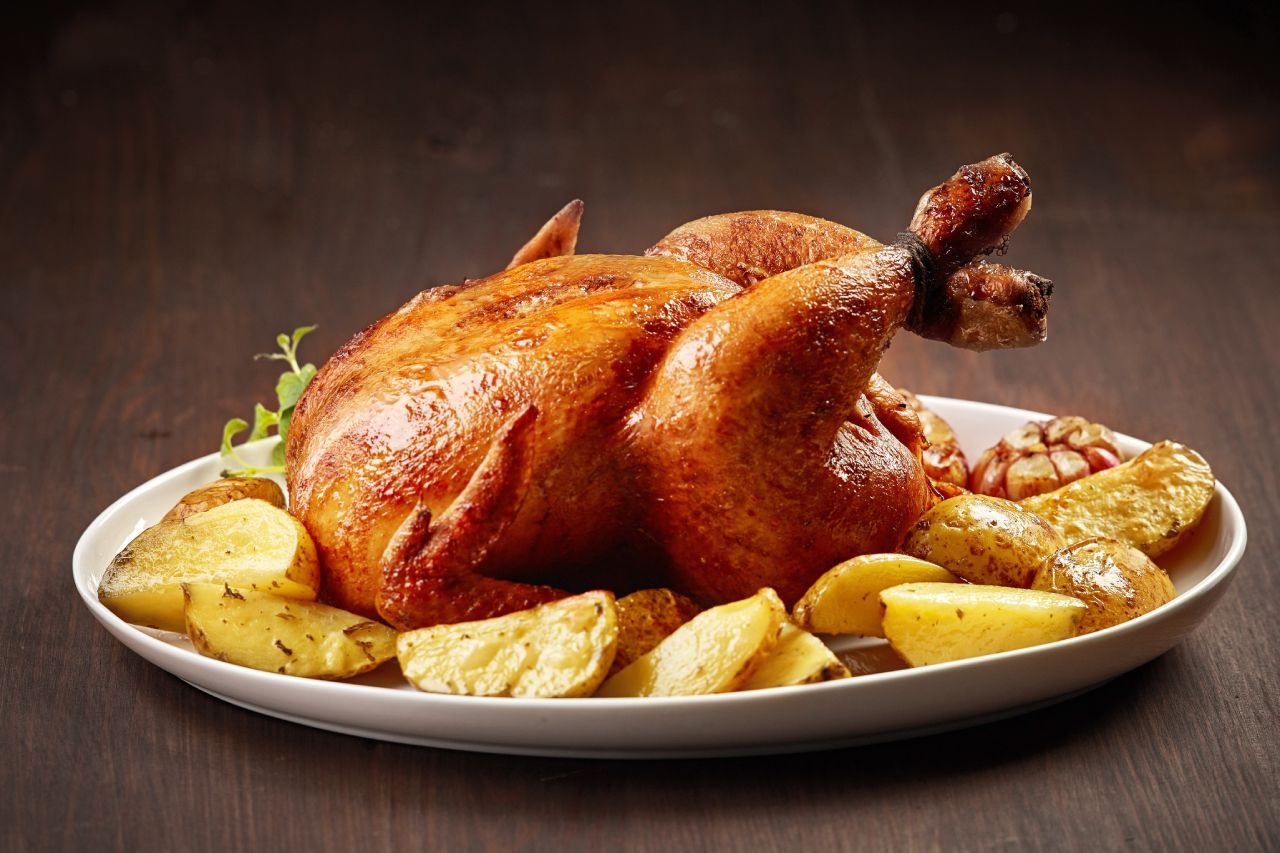 Um frango assado com batatas em um prato branco sobre uma mesa de madeira.