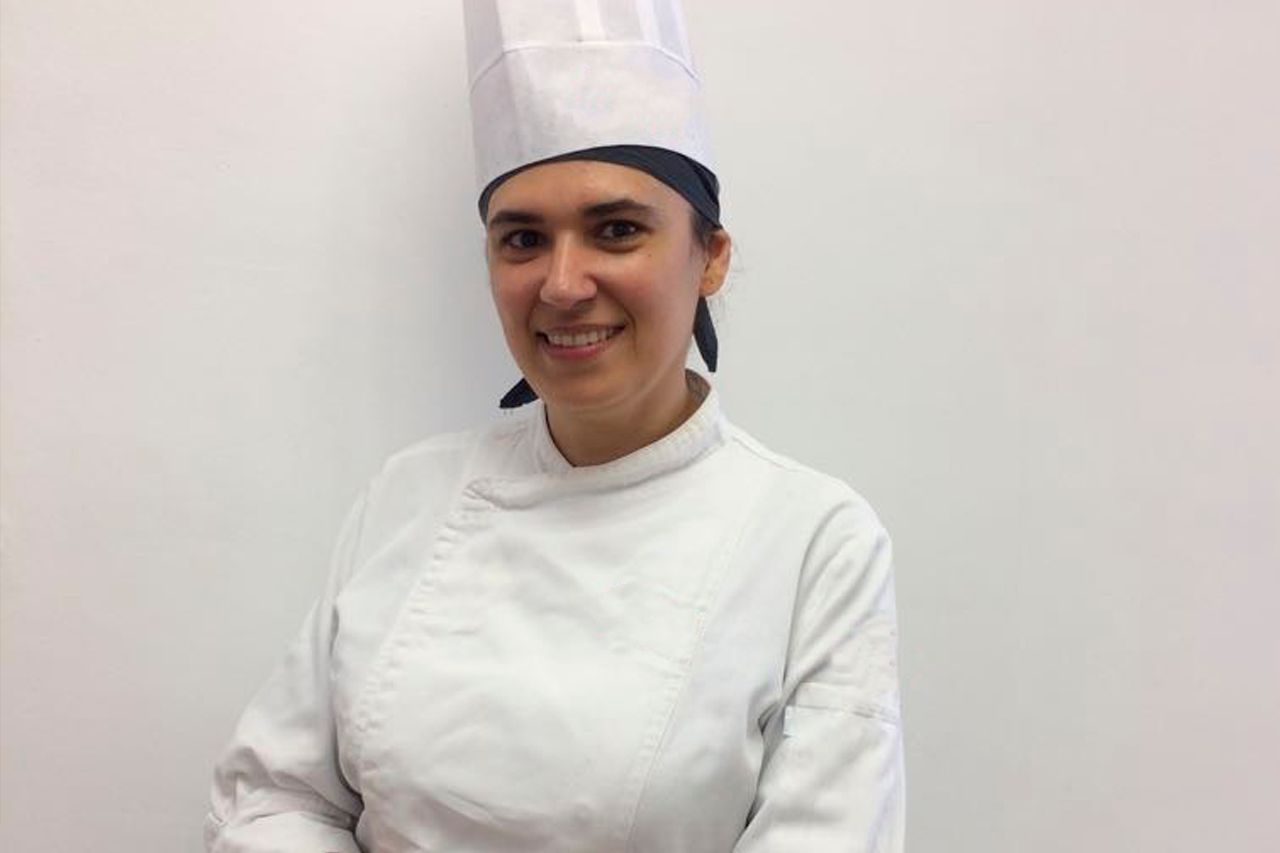 Uma mulher está usando um chapéu de chef e sorrindo.