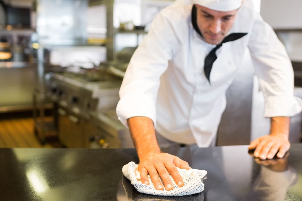 Um chef está limpando um balcão com uma toalha na cozinha.