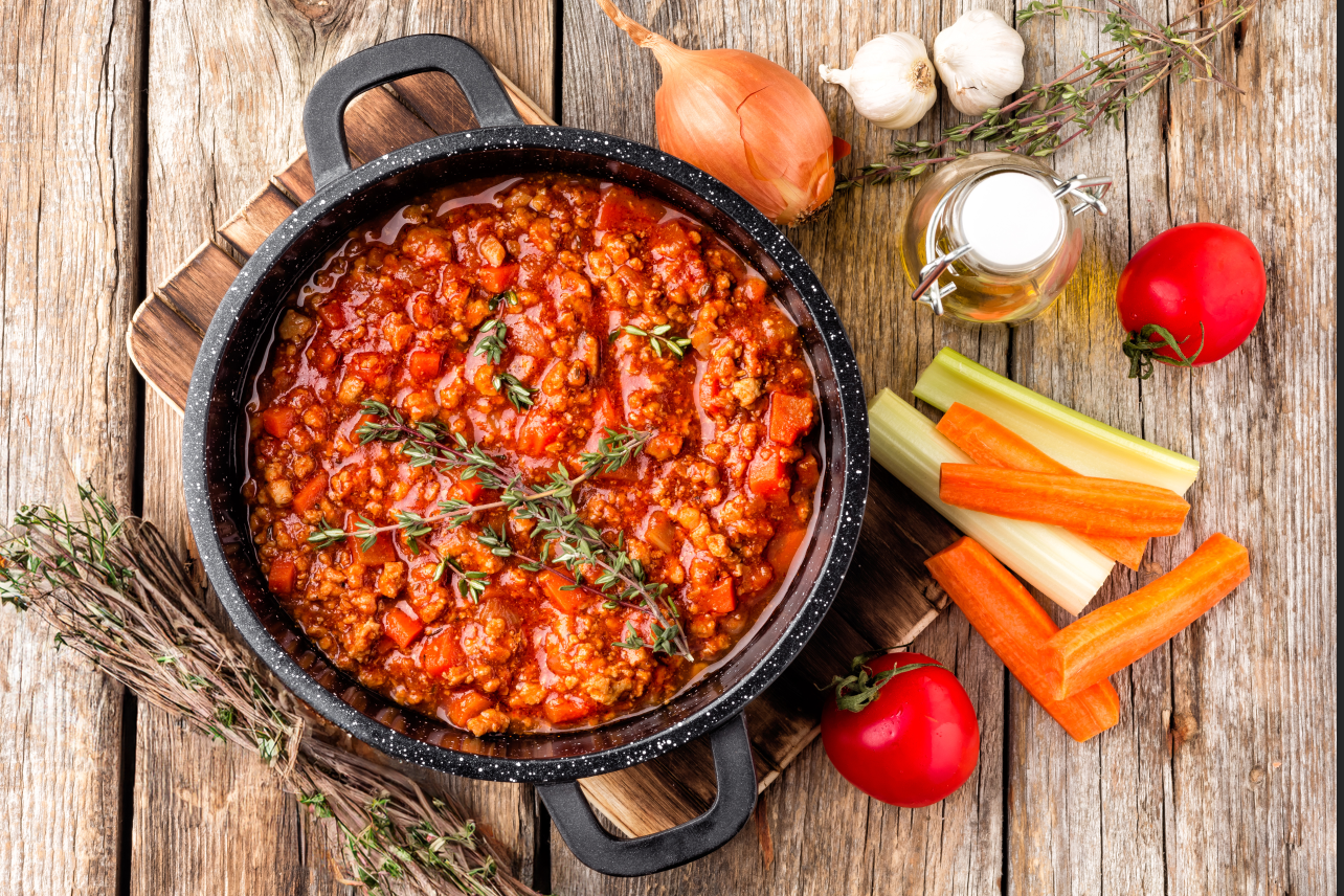 Uma panela de molho de carne à bolonhesa com cenouras e aipo sobre uma mesa de madeira.
