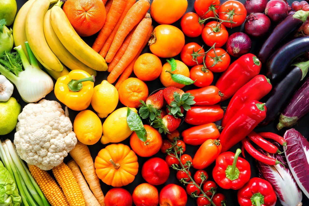 Uma variedade de frutas e vegetais estão dispostos em um padrão de arco-íris.