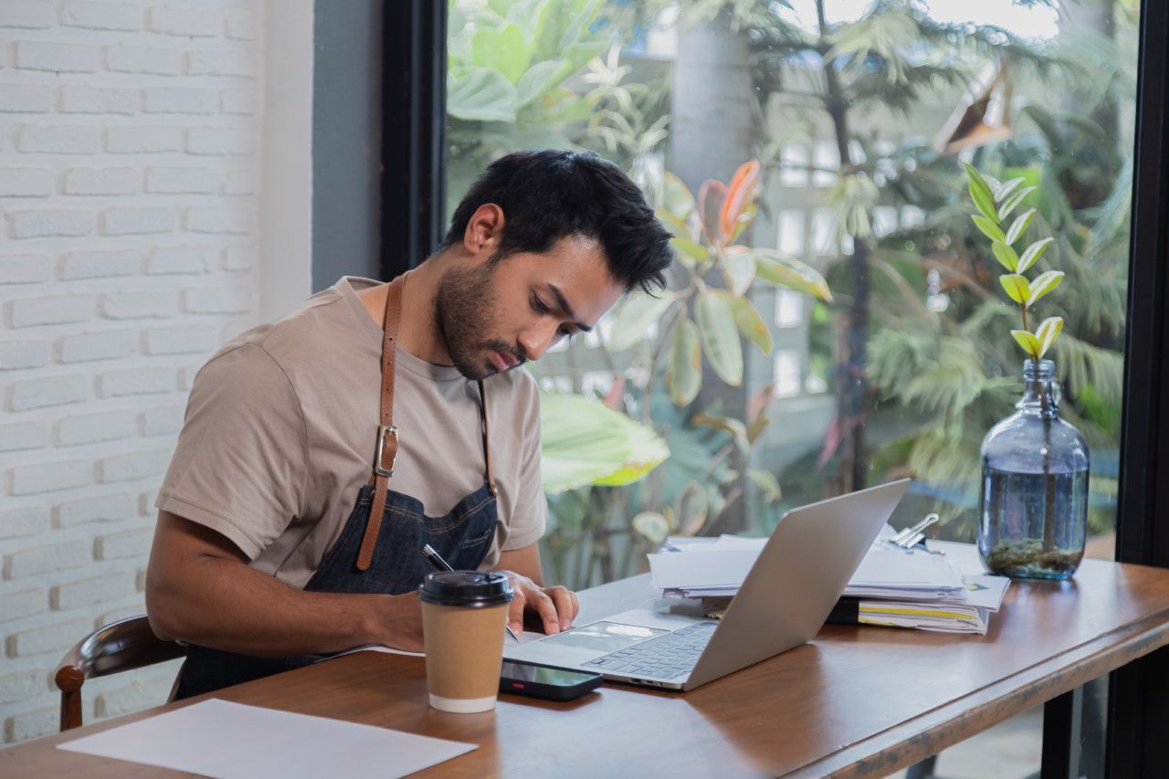 Um homem está sentado à mesa usando um laptop.