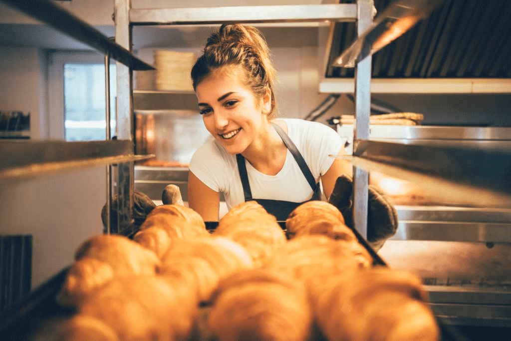 Uma mulher está olhando para uma bandeja de croissants em uma padaria.