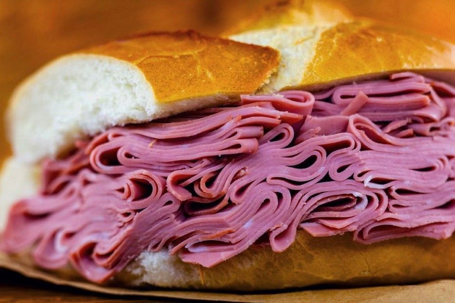 Um close de um sanduíche de pastrami em um pão sobre uma mesa.