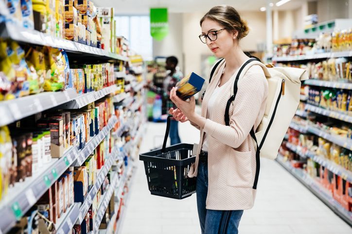 Uma mulher está parada em um supermercado olhando para uma garrafa de comida.