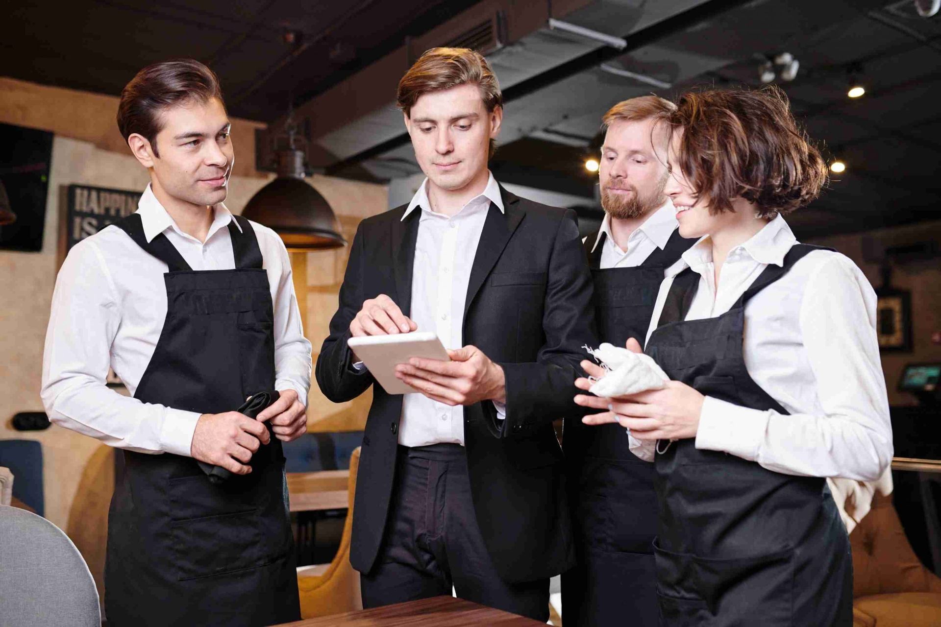 Um grupo de pessoas está em volta de uma mesa em um restaurante olhando para um tablet.