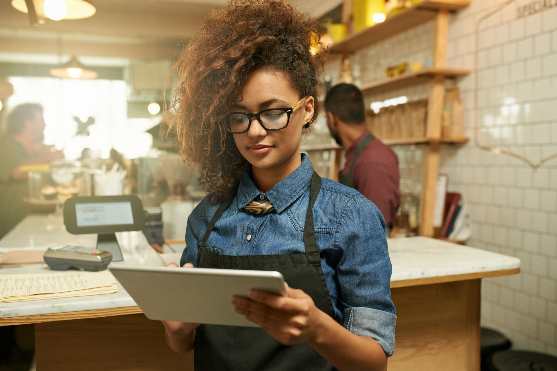 Uma mulher de avental está usando um tablet em um restaurante.