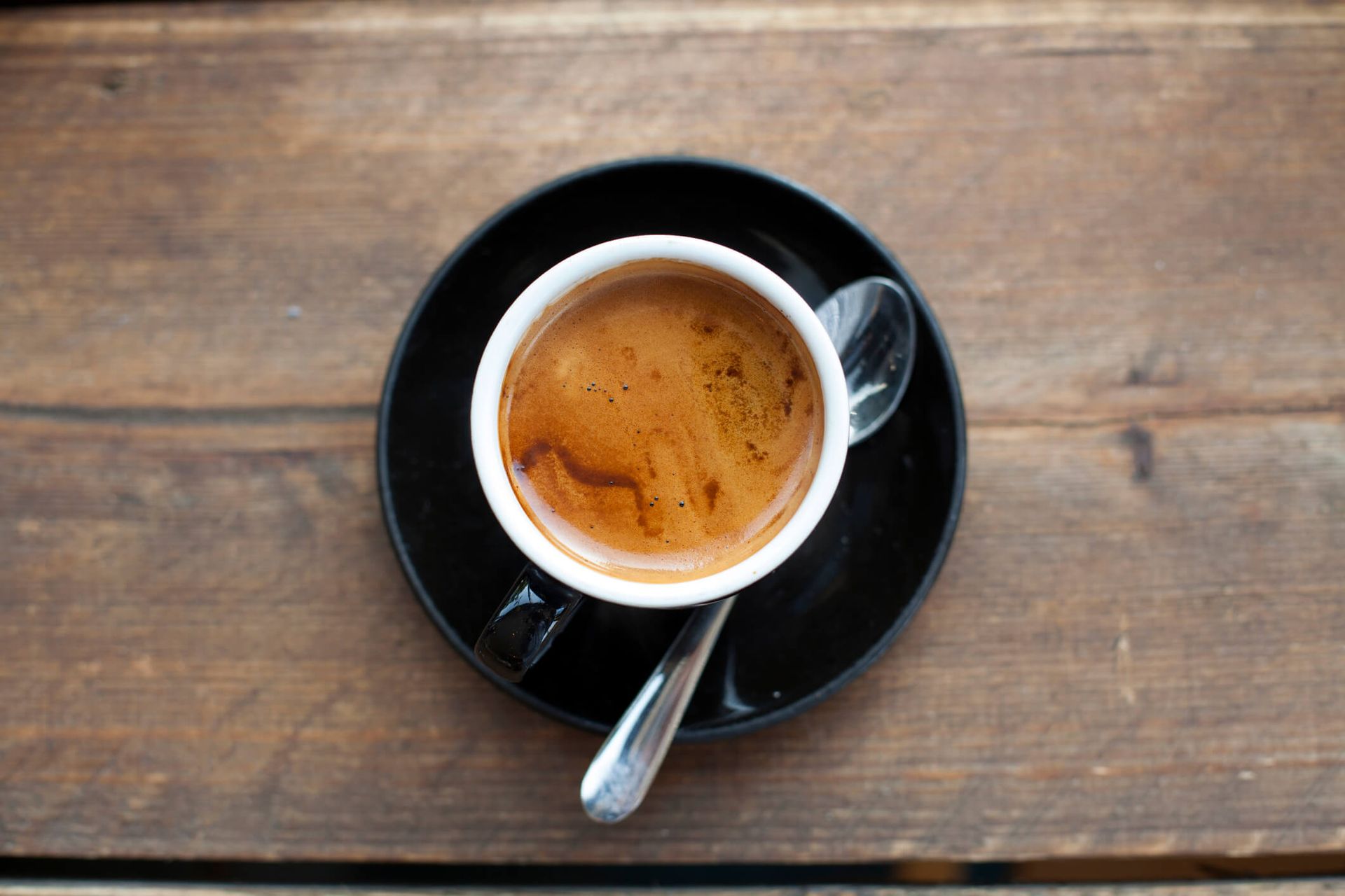 Uma xícara de café com uma colher em um pires sobre uma mesa de madeira.