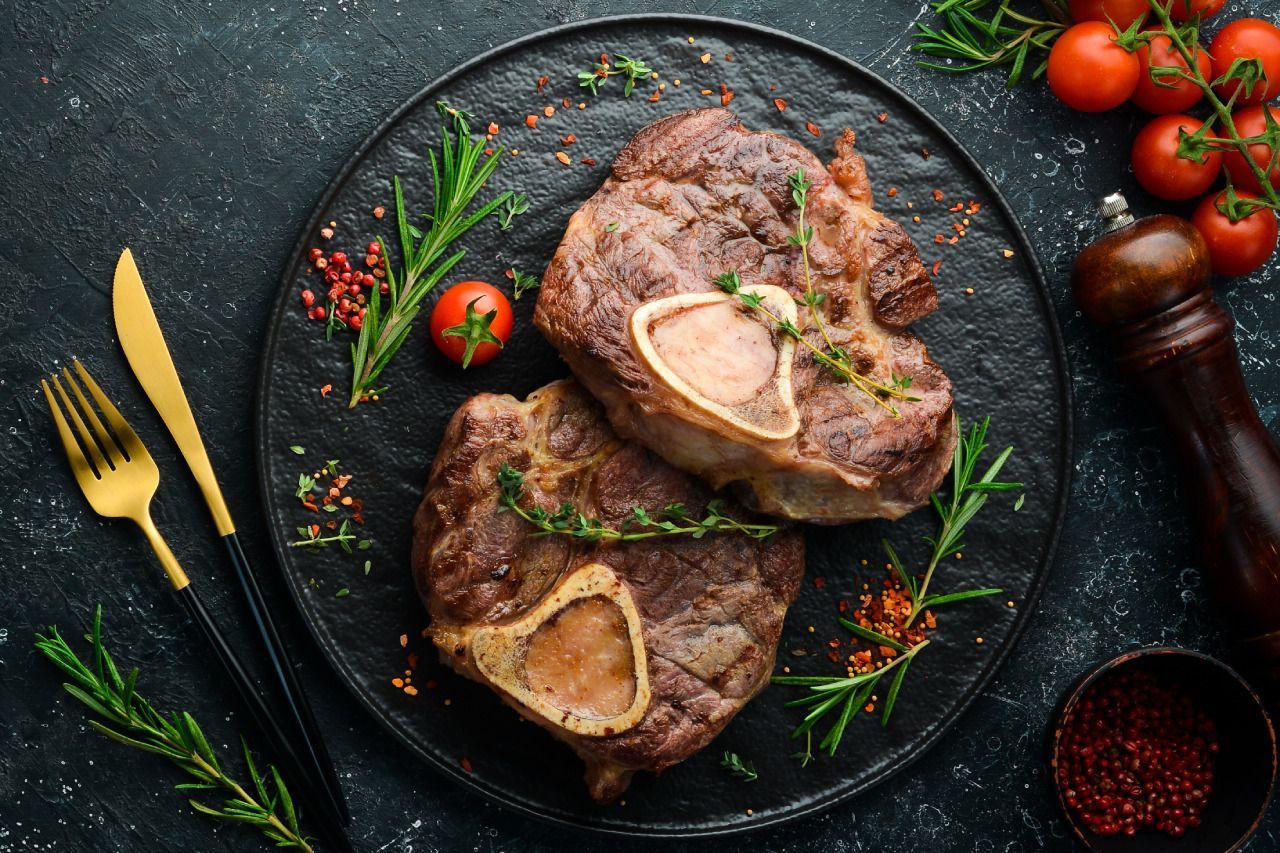 Um prato de carne com ossos e tomates sobre uma mesa.