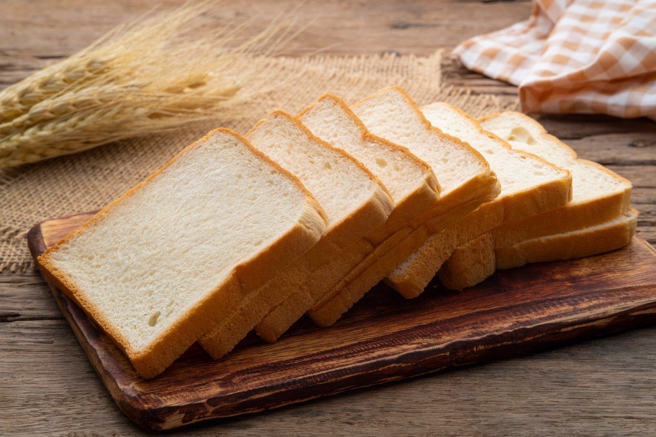 Fatias de pão branco estão sobre uma tábua de corte de madeira.