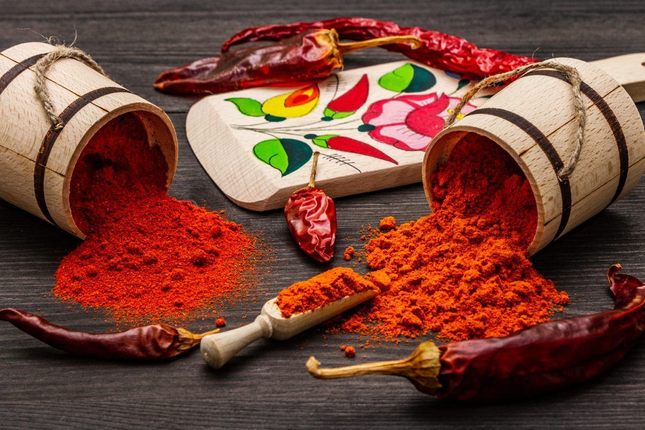 Uma mesa de madeira coberta com baldes de pimenta vermelha em pó e pimentas secas.
