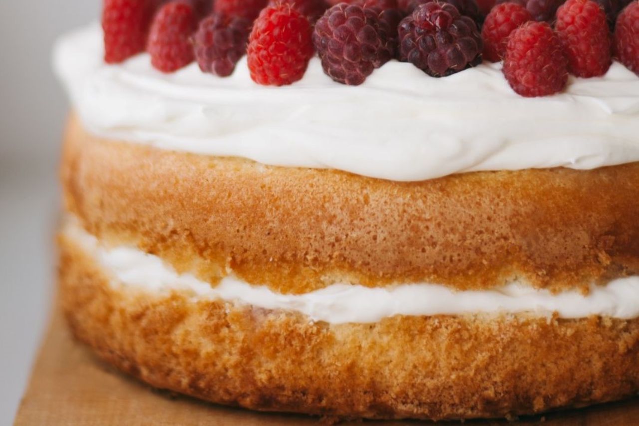 Um close de um bolo com framboesas e chantilly por cima.