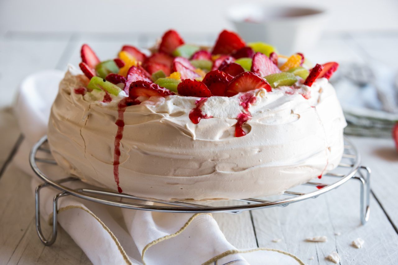 Um bolo com chantilly e frutas por cima está em uma grade para esfriar.