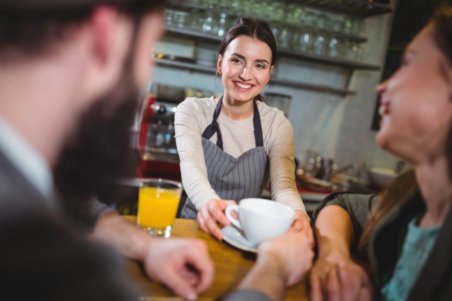 Uma garçonete está servindo uma xícara de café para duas pessoas em um restaurante.