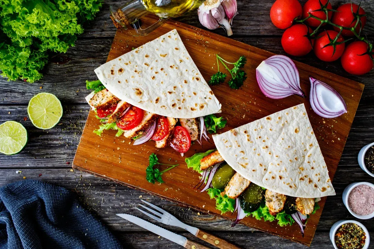 Piadinas recheadas com frango grelhado, tomate, alface e cebola roxa sobre tábua de madeira