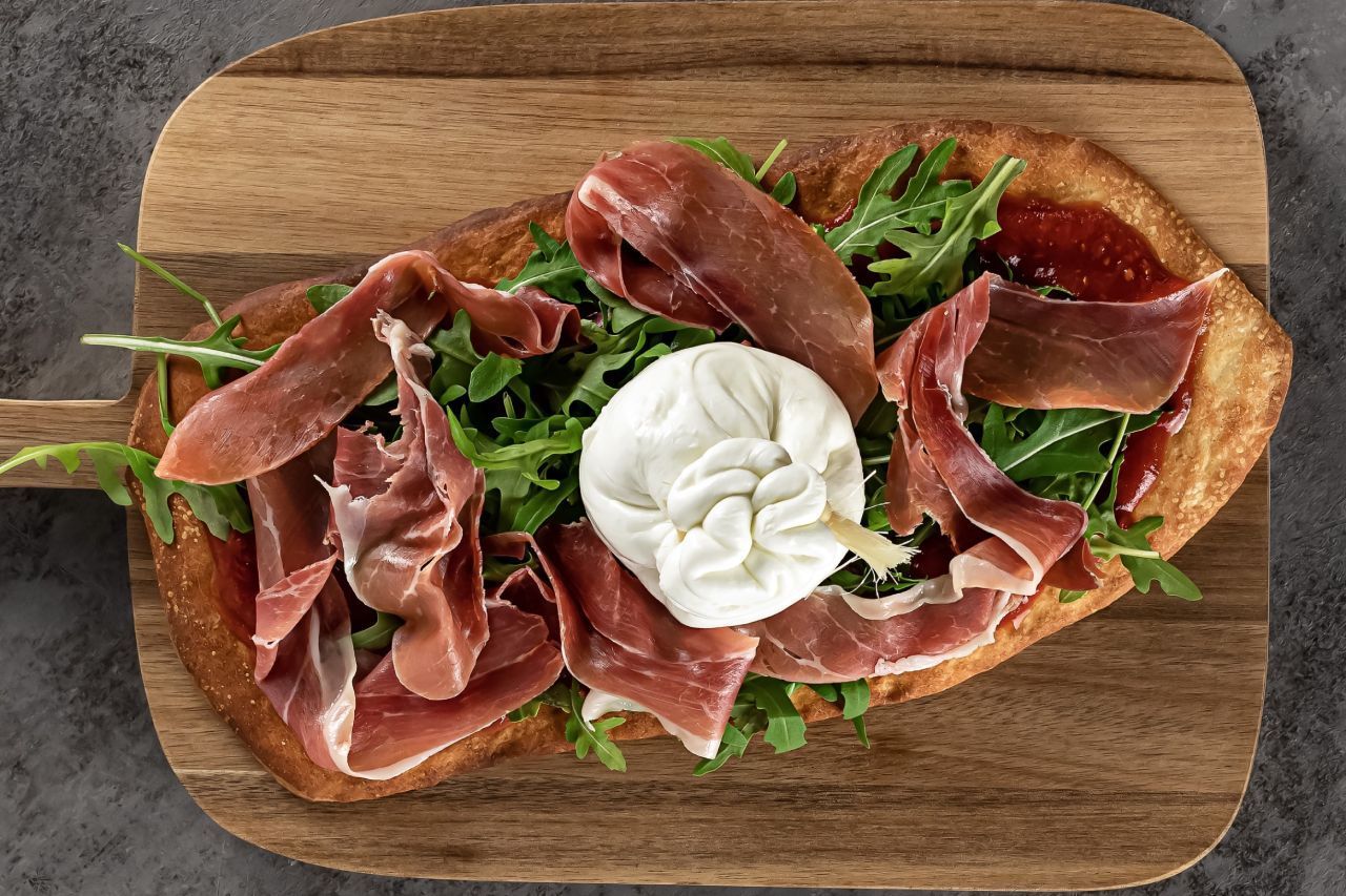 Uma pizza com carne e queijo em uma tábua de corte de madeira.