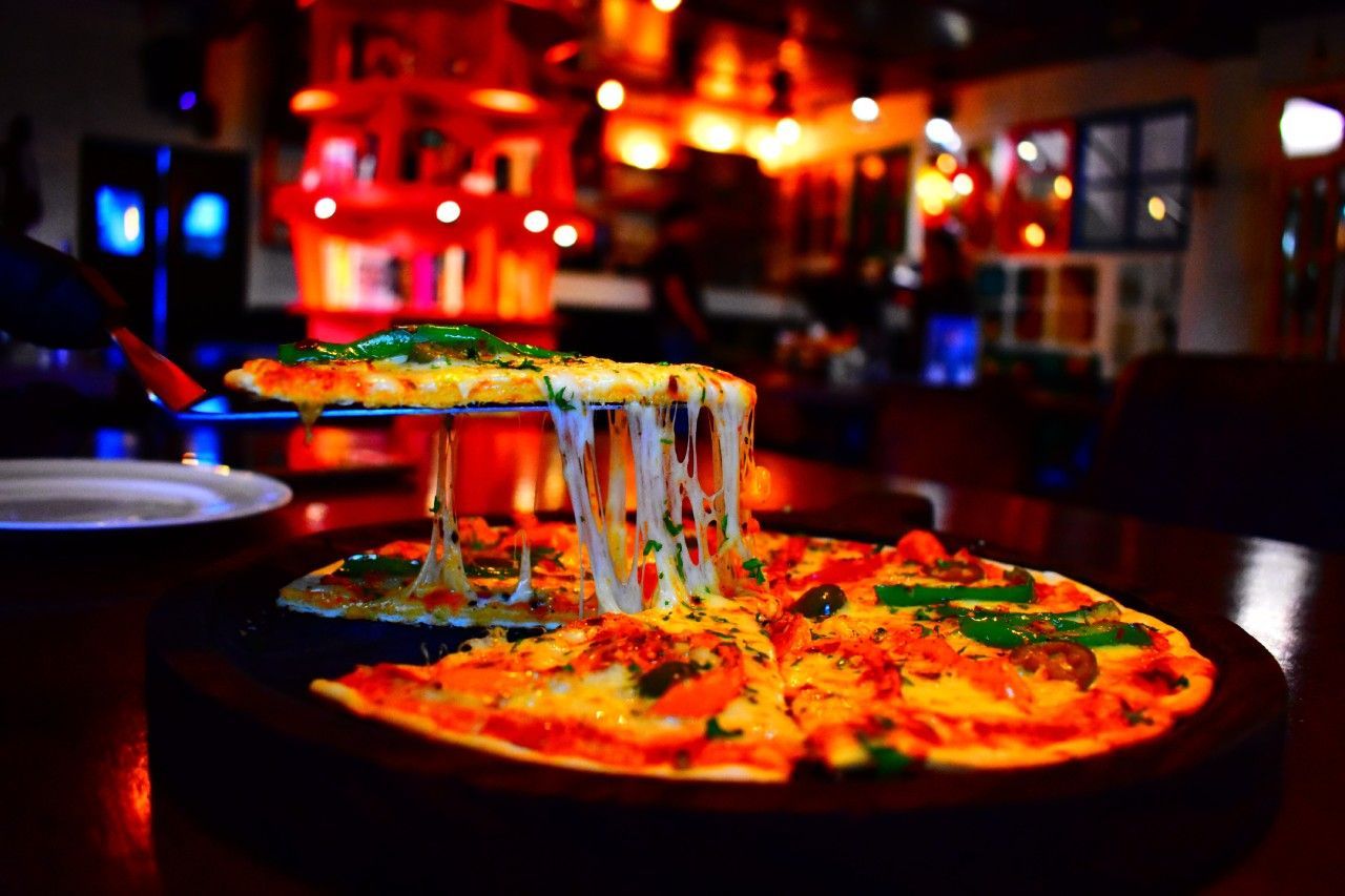 Uma pizza com queijo saindo dela está sobre uma mesa em um restaurante.