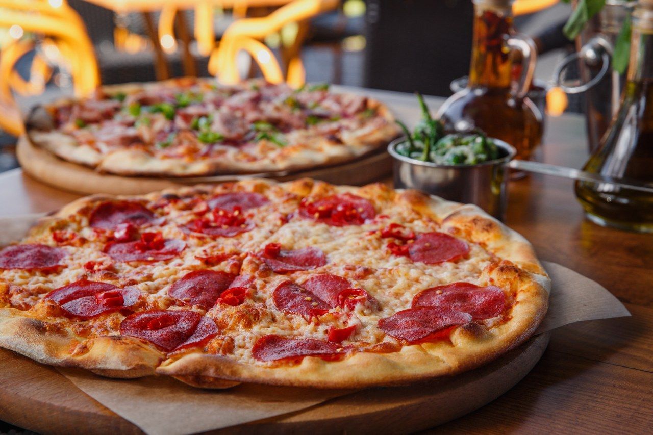 Duas pizzas estão sobre uma tábua de madeira em cima da mesa.