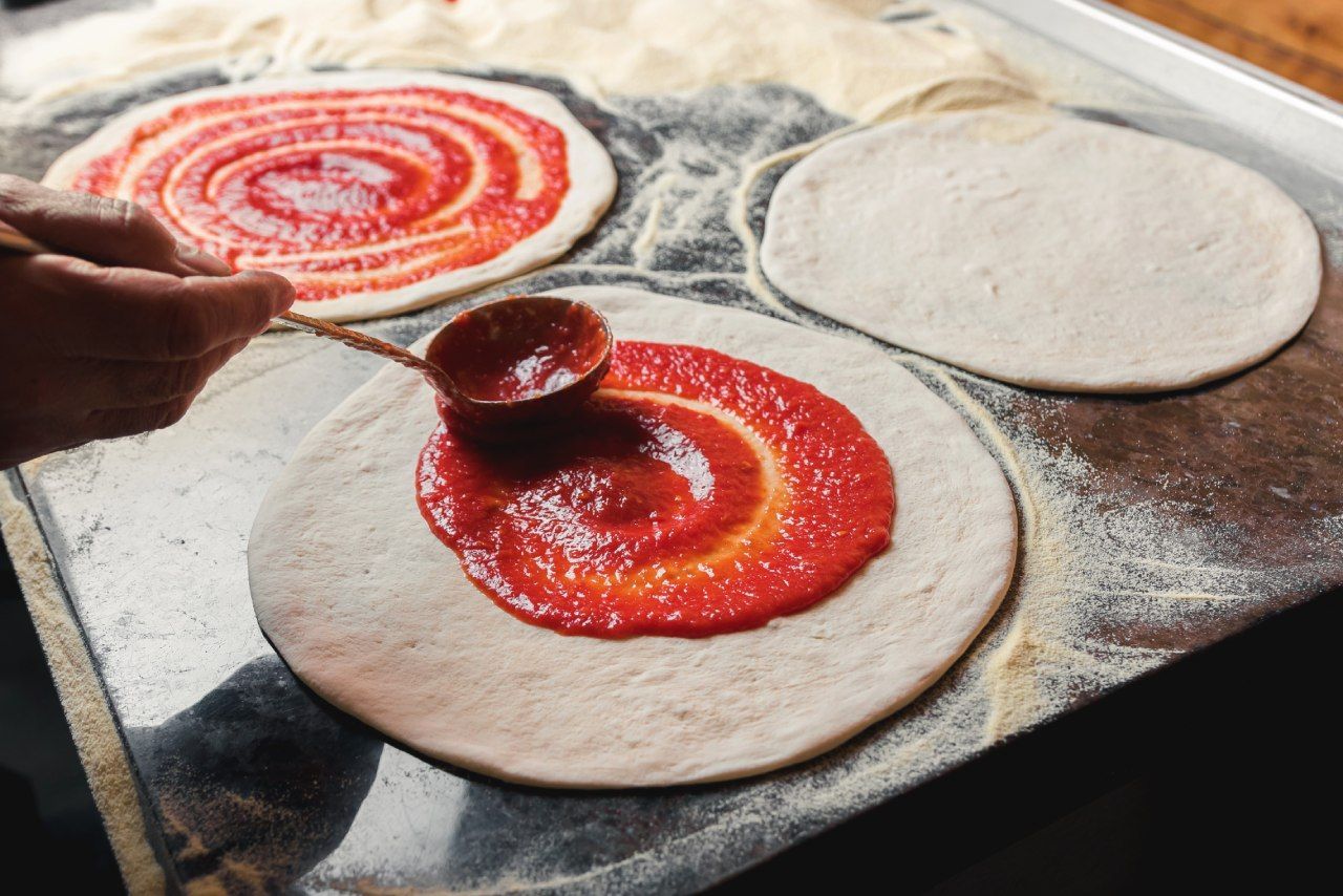 Uma pessoa está espalhando molho de tomate na massa de uma pizza.