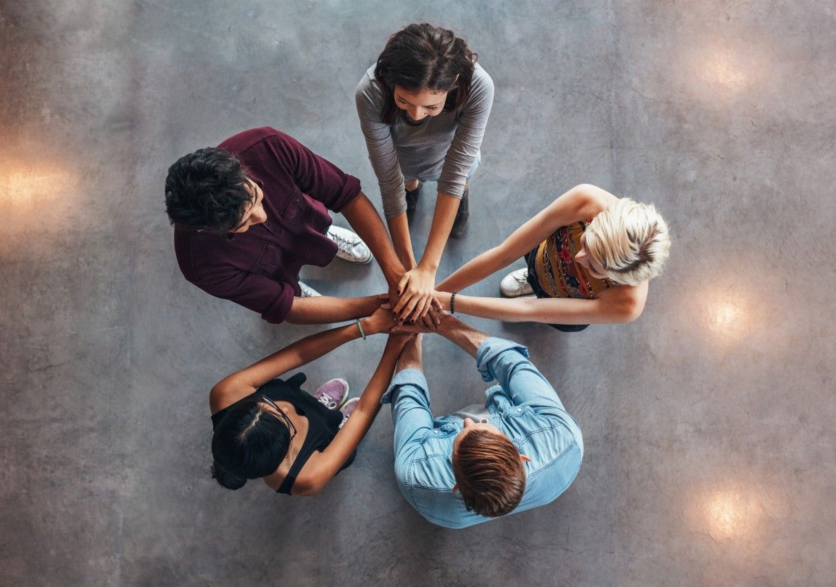 Um grupo de pessoas está juntando as mãos em um círculo.