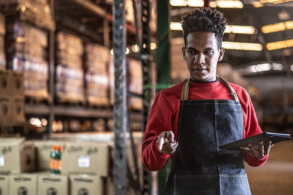 Um homem de avental está segurando um tablet em um depósito.