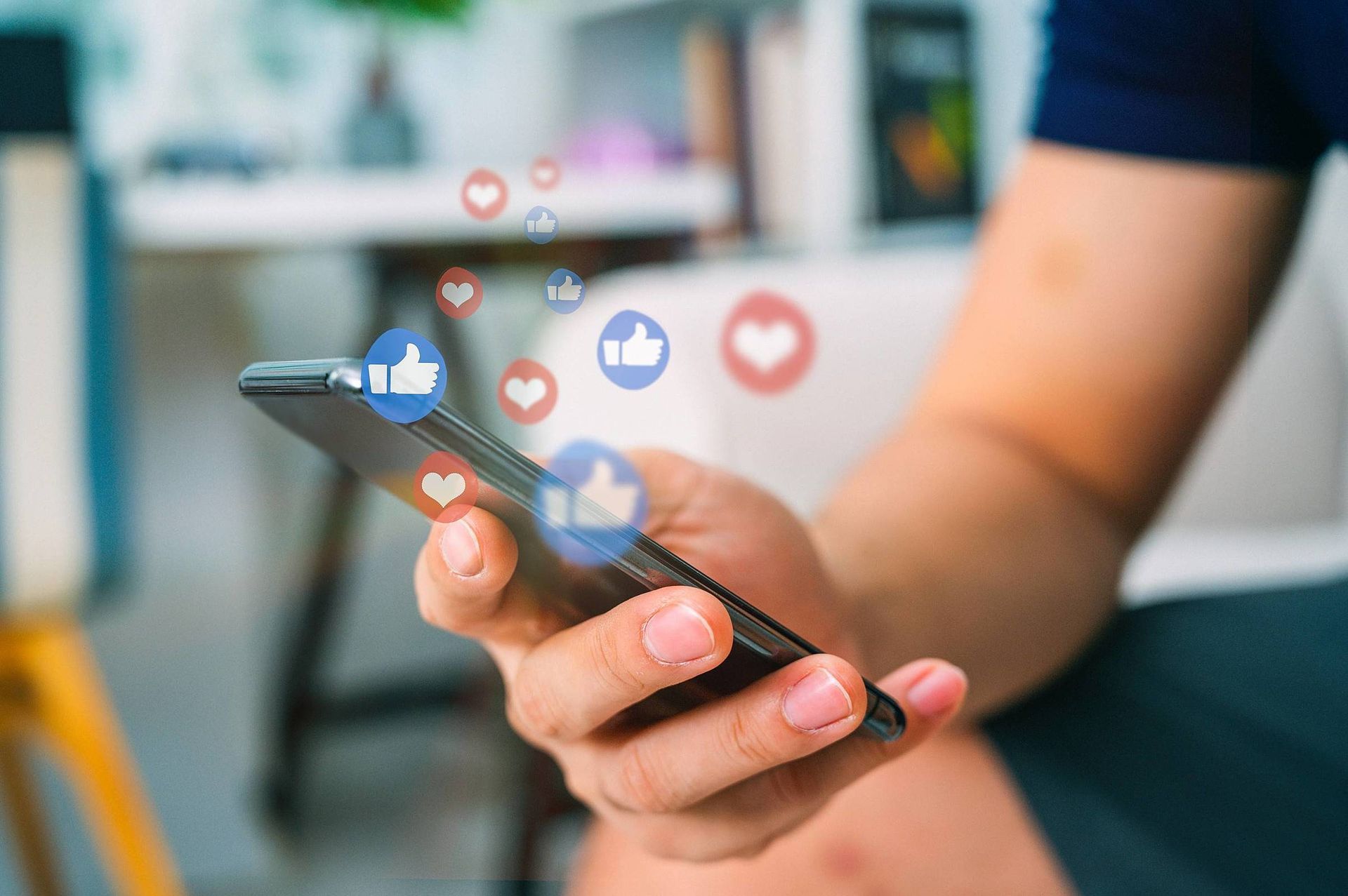 Uma pessoa está segurando um celular na mão com ícones de mídia social saindo dele.