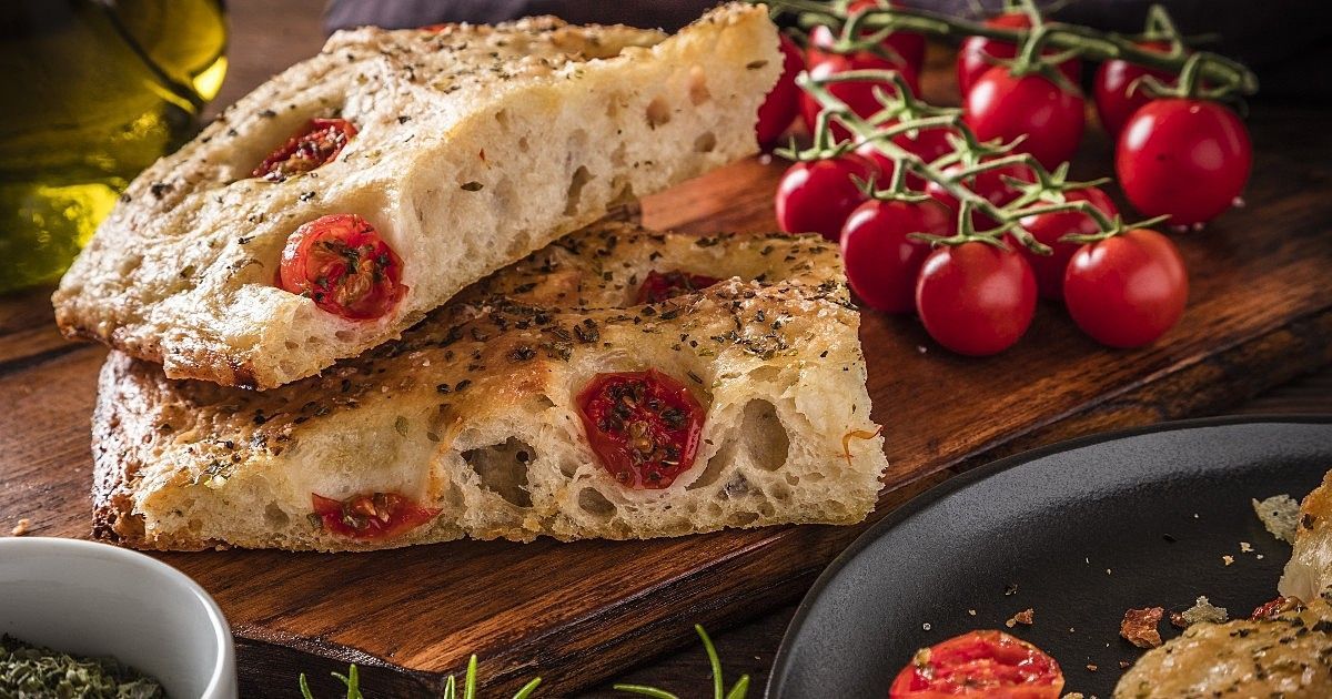Uma fatia de pão com tomates está sobre uma tábua de corte de madeira.