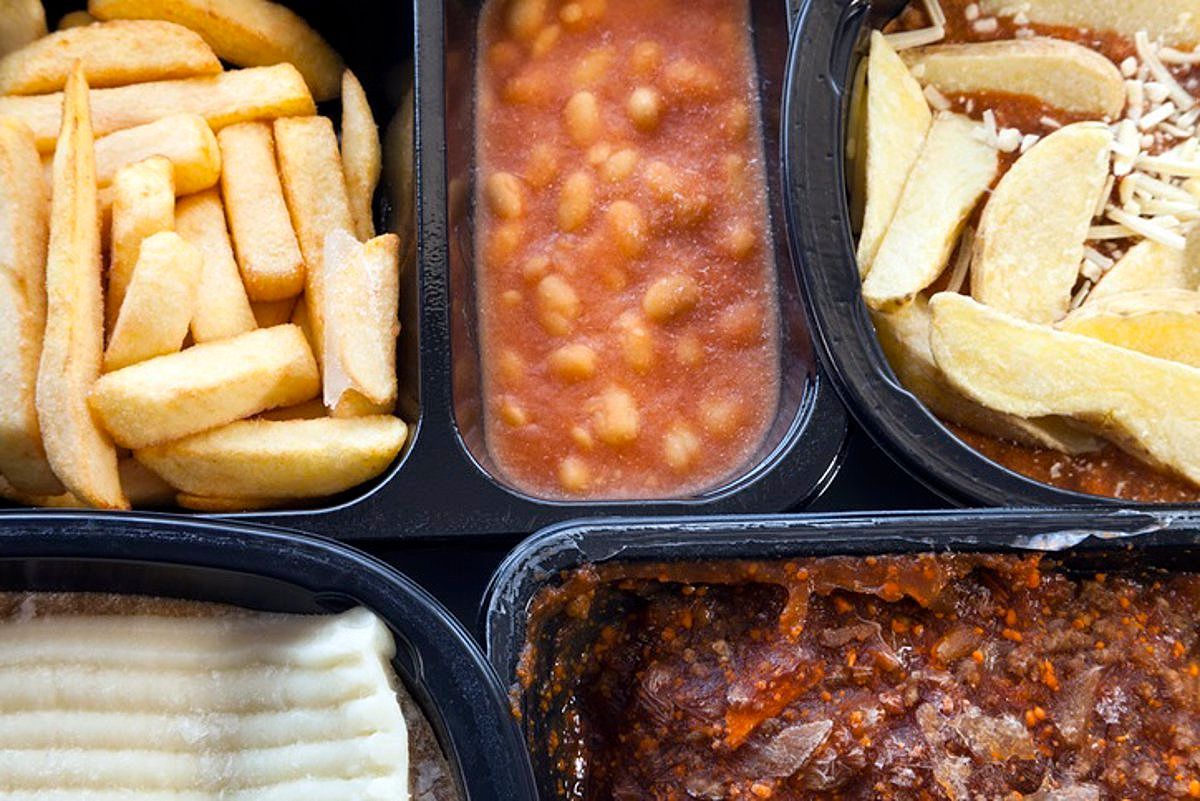 Um close de uma bandeja de comida com batatas fritas, feijão, almôndegas e purê de batatas.