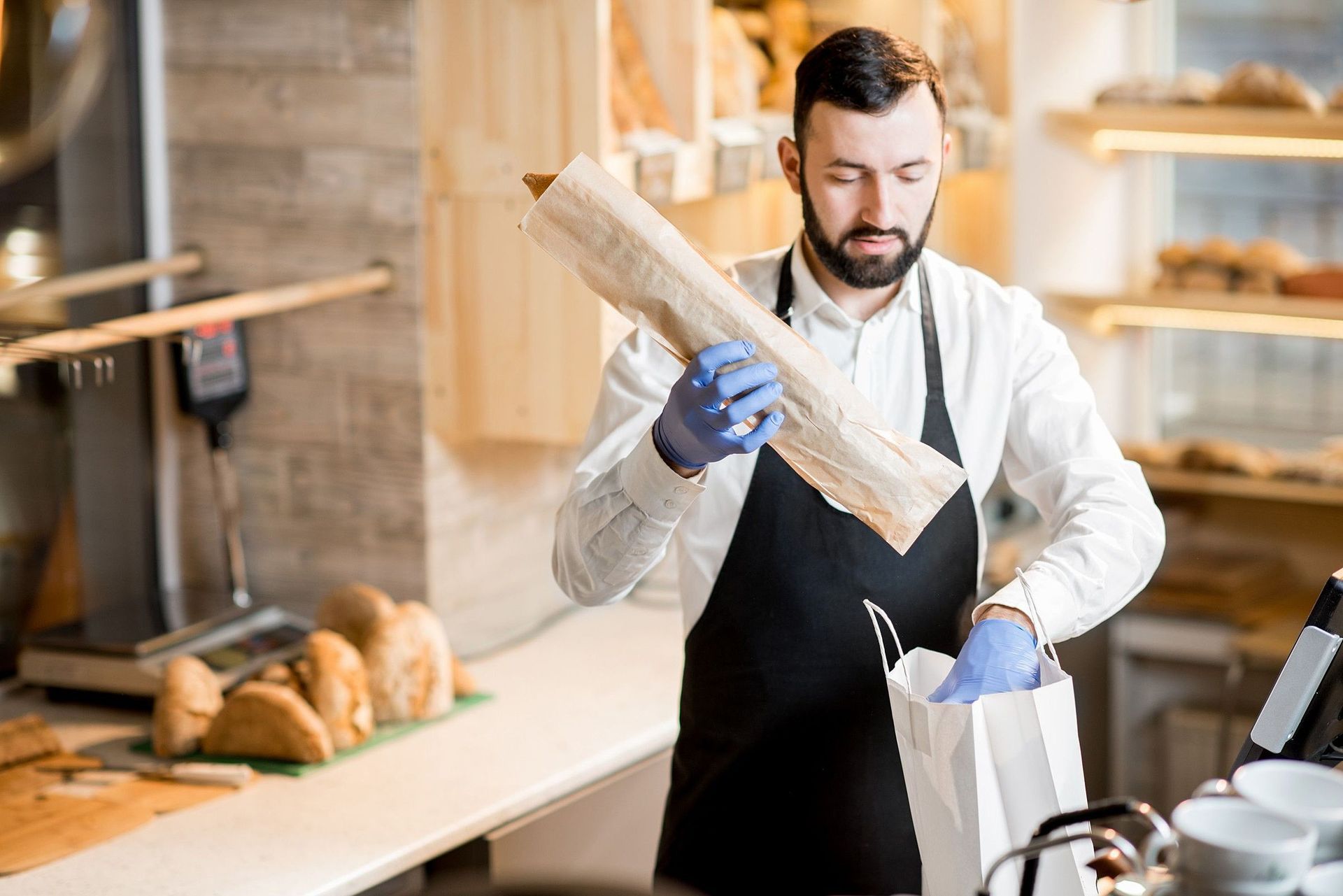 Um homem de avental está segurando uma baguete em uma padaria.