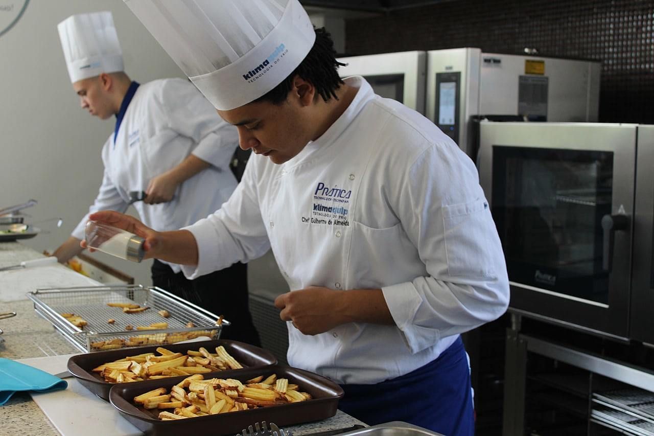 Um homem com chapéu de chef está preparando comida em uma cozinha