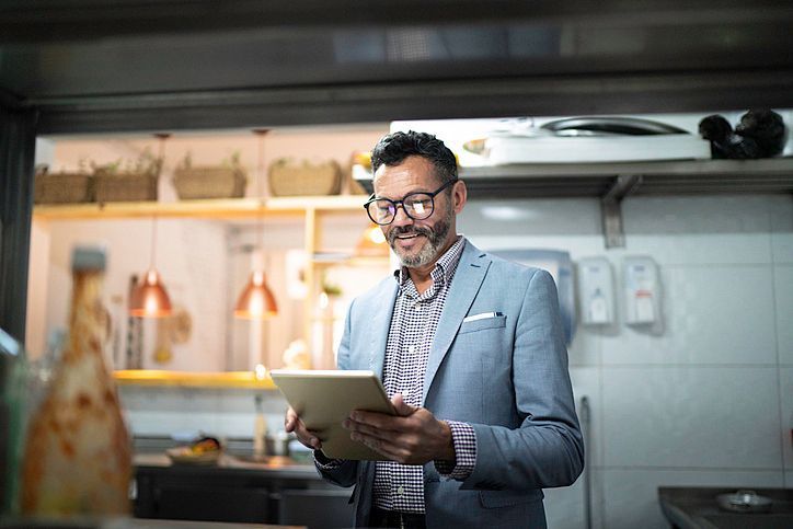 Um homem de terno está segurando um tablet na cozinha.