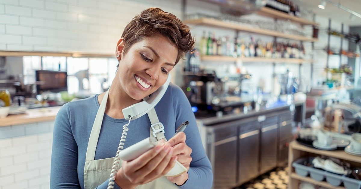 Uma mulher está falando ao telefone em um restaurante enquanto segura um tablet.