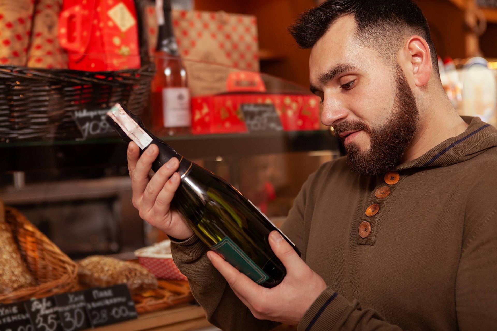 Um homem com barba está segurando uma garrafa de vinho em uma loja.