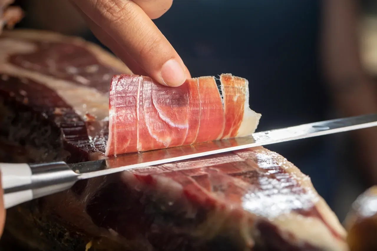 Fatia de jamón ibérico sendo cortada manualmente com faca longa