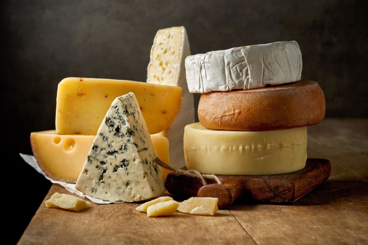 Queijos variados sobre tábua de madeira, incluindo queijo azul com veios, queijo de casca branca tipo brie, peças semiduras e lascas de queijo curado.