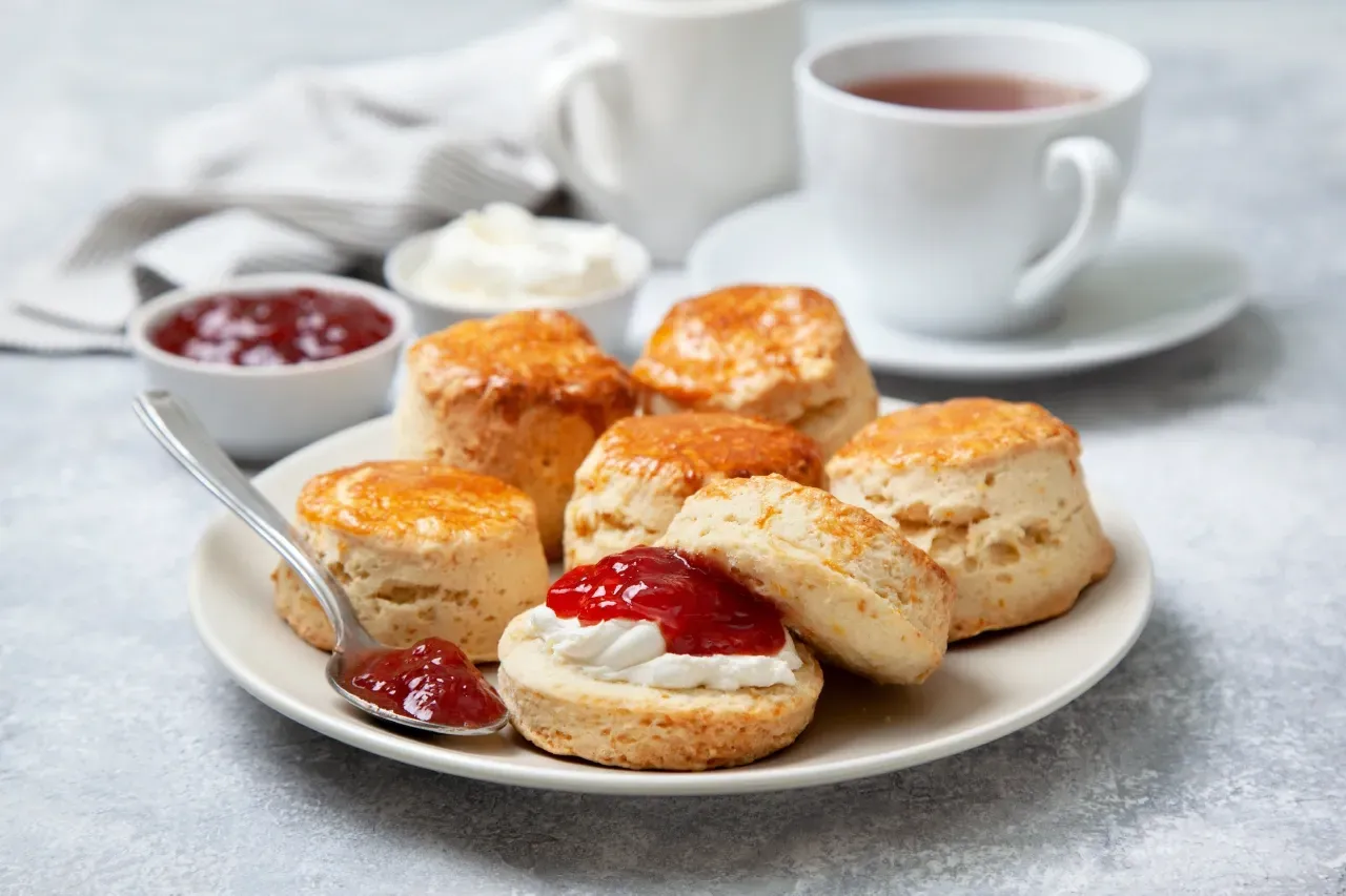 Scones com clotted cream geleia e chá sobre mesa cinza

