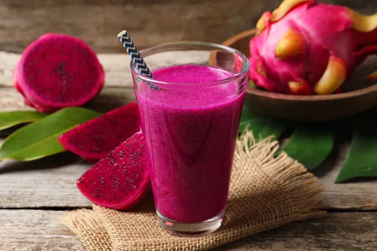 Smoothie ou suco de pitaya vermelha com pitayas ao fundo sobre mesa de madeira.