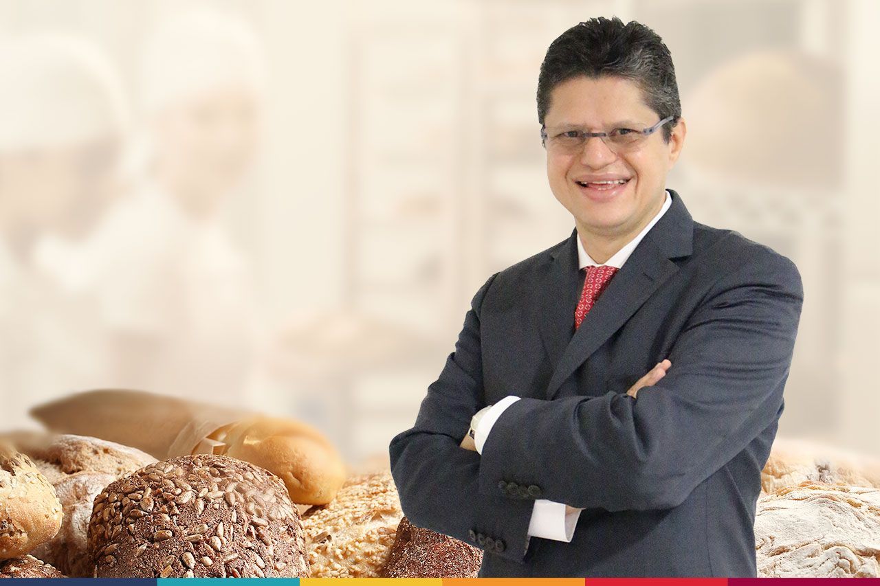 Um homem de terno e gravata está parado em frente a uma pilha de pão