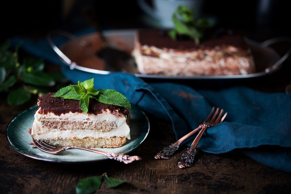 Um pedaço de bolo tiramisu em um prato com um garfo e uma colher.