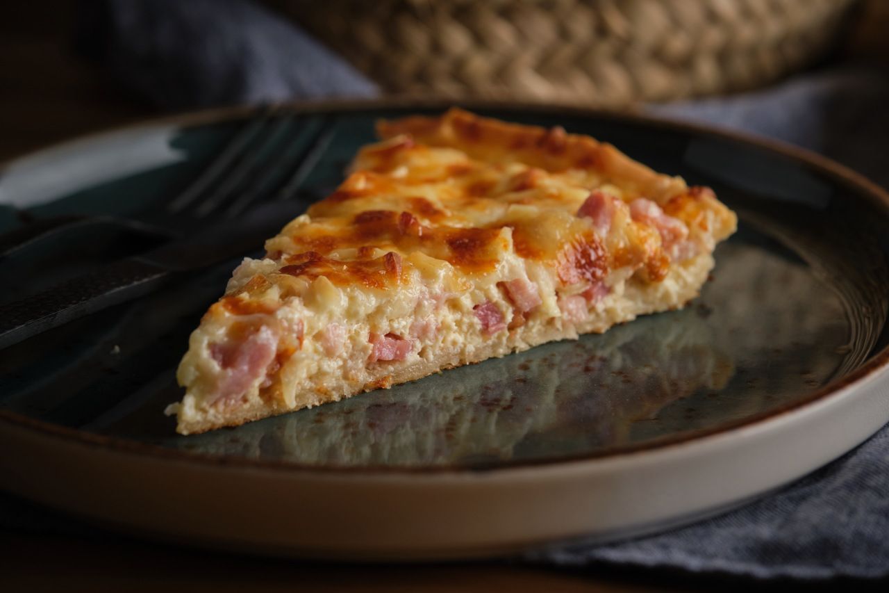 Uma fatia de quiche está em um prato com um garfo.
