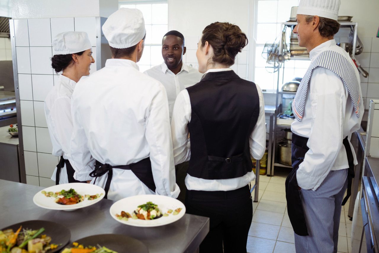 Um grupo de chefs estão em uma cozinha conversando entre si.