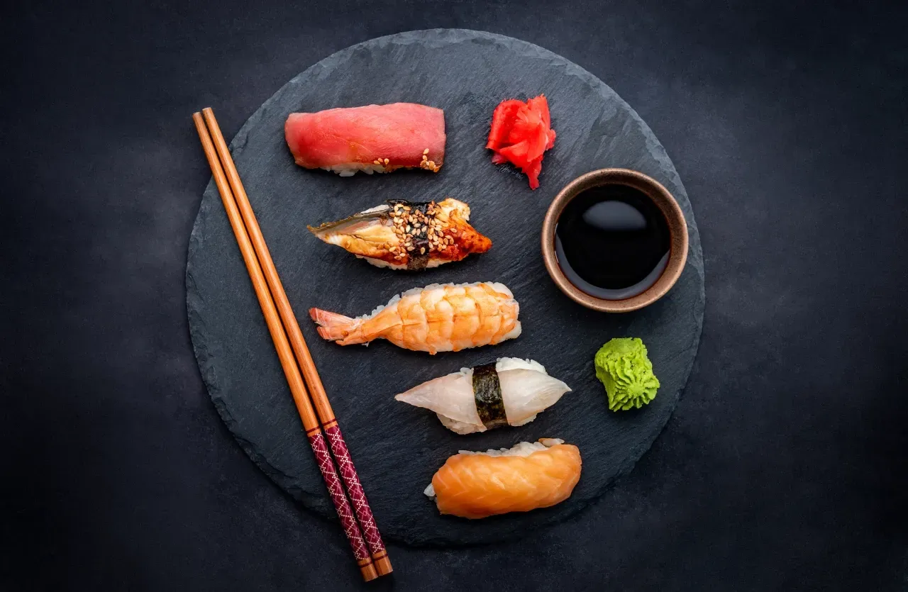 Um prato de sushi com pauzinhos e uma tigela de molho de soja.