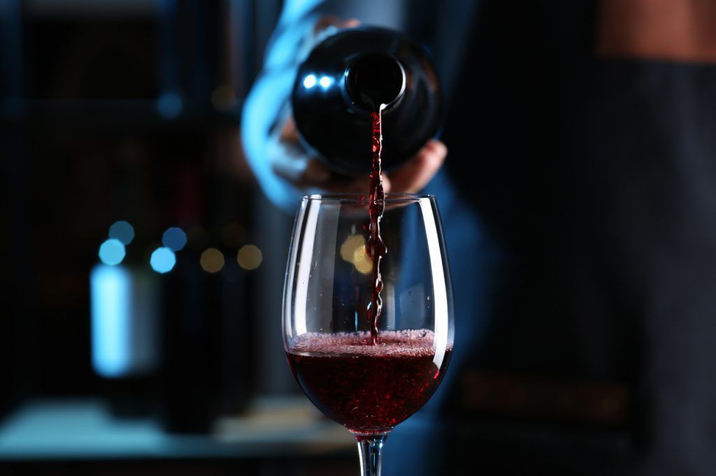 Uma pessoa está despejando vinho tinto em uma taça.